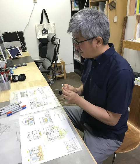 エムプラス建築工房の一級建築士平松優司がデスクで建築設計図を書いている様子